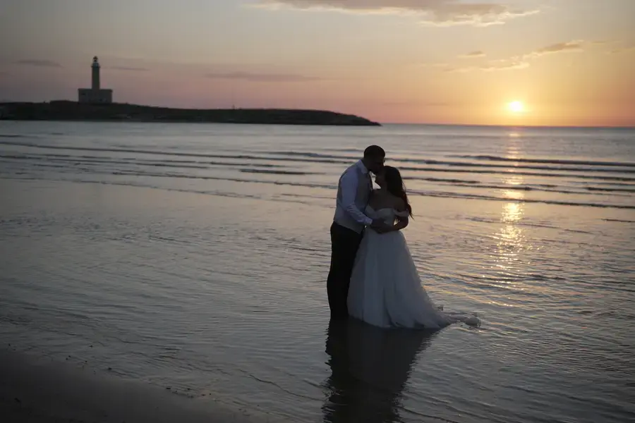 Gli sposi in acqua al tramonto con il faro sullo sfondo