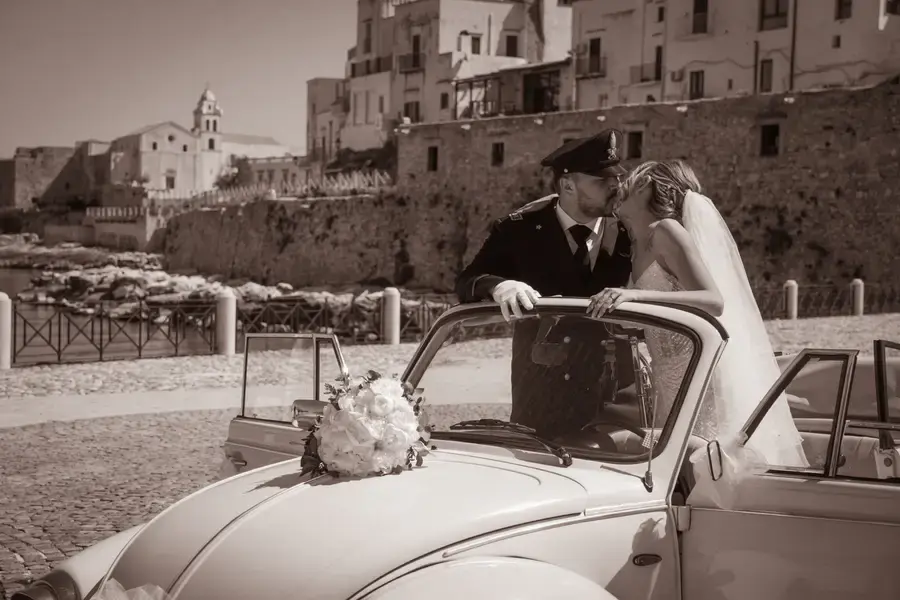 Gli sposi accanto all'auto d'epoca davanti al borgo, in bianco e nero