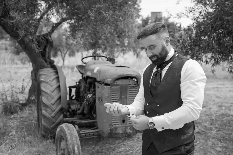 Lo sposo sorride accanto a un trattore, in bianco e nero