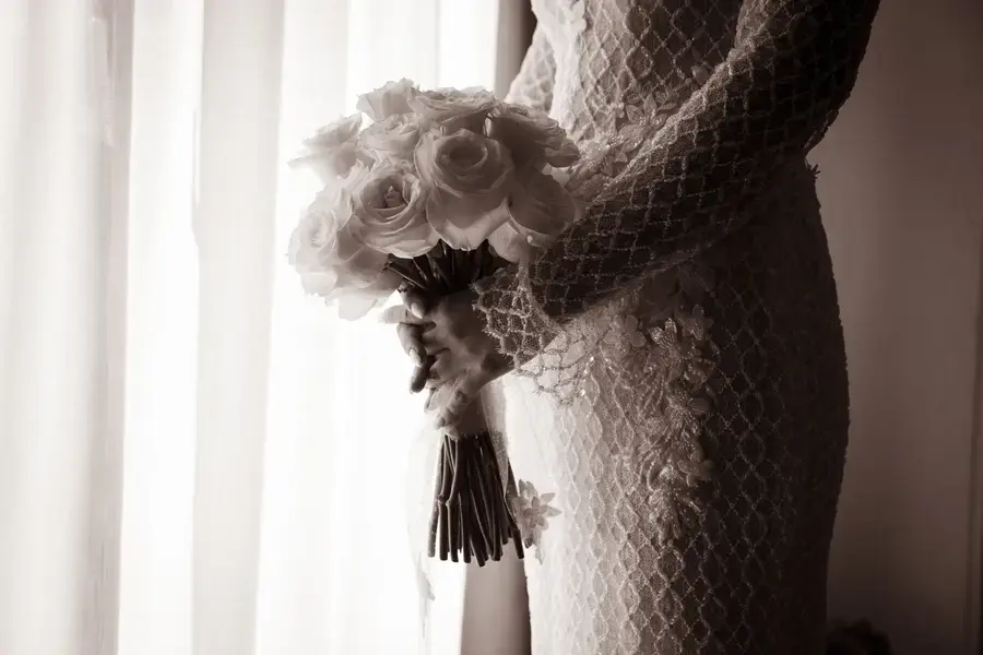 La sposa stringe il bouquet davanti alla tenda bianca