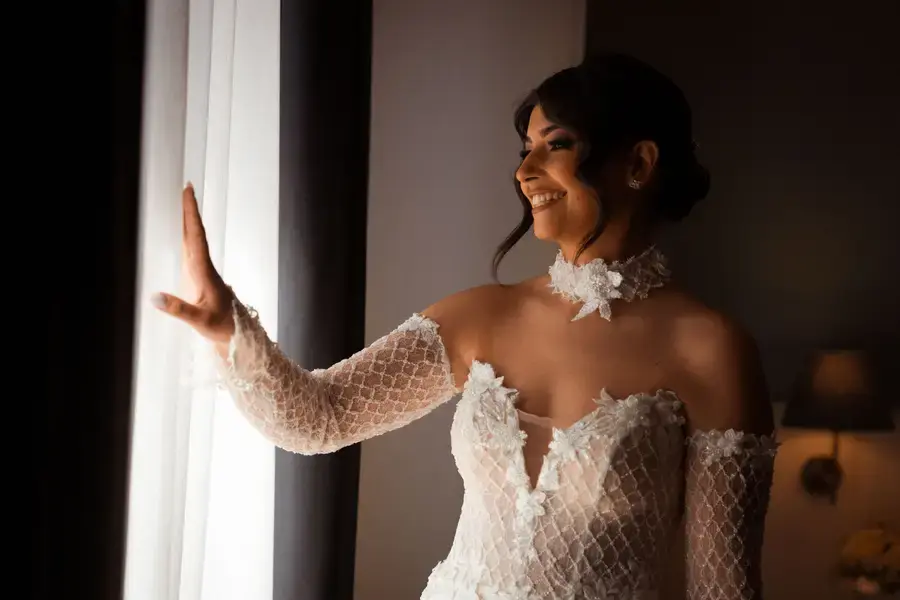 La sposa sorride scostando la tenda della finestra